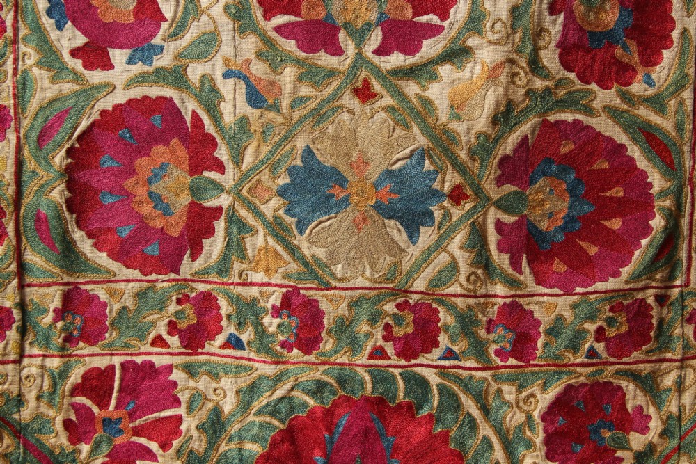 A rectangular hand-embroidered antique Suzani textile featuring red and pink floral medallions on a cream background with green vine borders. View VII