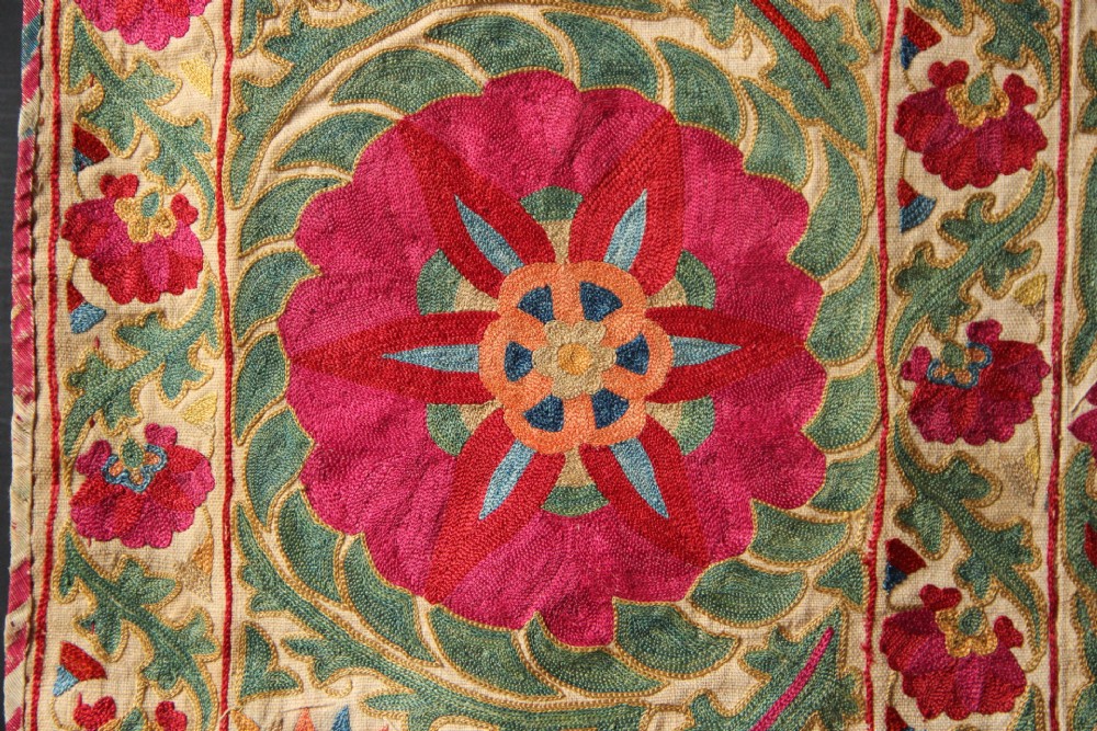 A rectangular hand-embroidered antique Suzani textile featuring red and pink floral medallions on a cream background with green vine borders. View VIII