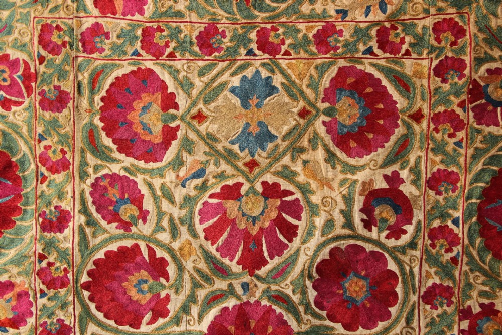 A rectangular hand-embroidered antique Suzani textile featuring red and pink floral medallions on a cream background with green vine borders. View IX