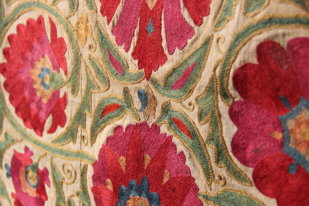 A rectangular hand-embroidered antique Suzani textile featuring red and pink floral medallions on a cream background with green vine borders. View XII
