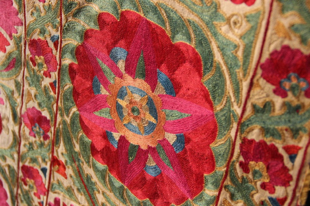 A rectangular hand-embroidered antique Suzani textile featuring red and pink floral medallions on a cream background with green vine borders. View XIII