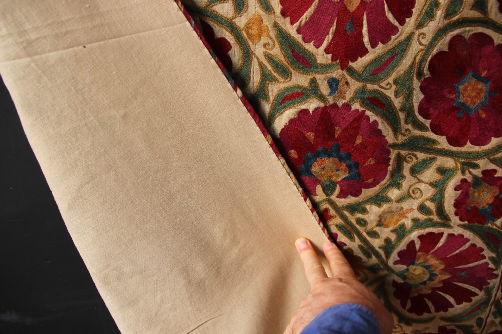 A rectangular hand-embroidered antique Suzani textile featuring red and pink floral medallions on a cream background with green vine borders. View XIV