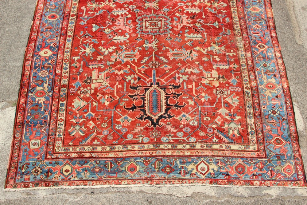An antique Persian Bakshaish wool carpet featuring a terracotta red field with geometric central motifs enclosed by a light blue patterned border. View II