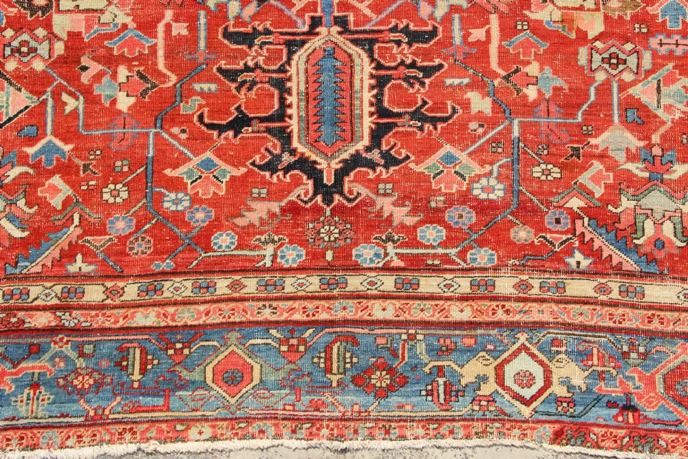 An antique Persian Bakshaish wool carpet featuring a terracotta red field with geometric central motifs enclosed by a light blue patterned border. View III