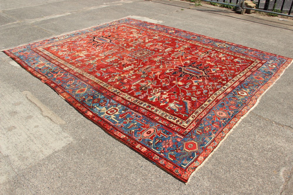 An antique Persian Bakshaish wool carpet featuring a terracotta red field with geometric central motifs enclosed by a light blue patterned border. View VI