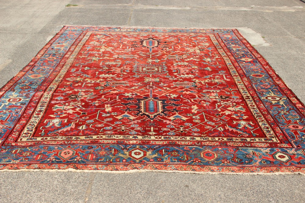 An antique Persian Bakshaish wool carpet featuring a terracotta red field with geometric central motifs enclosed by a light blue patterned border. View VII