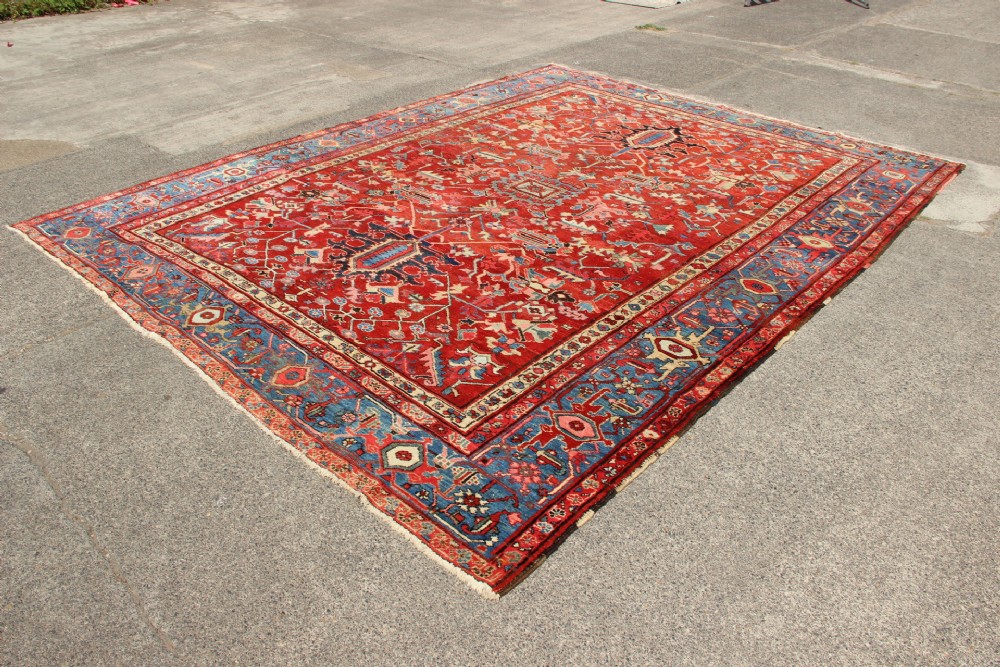 An antique Persian Bakshaish wool carpet featuring a terracotta red field with geometric central motifs enclosed by a light blue patterned border. View VIII