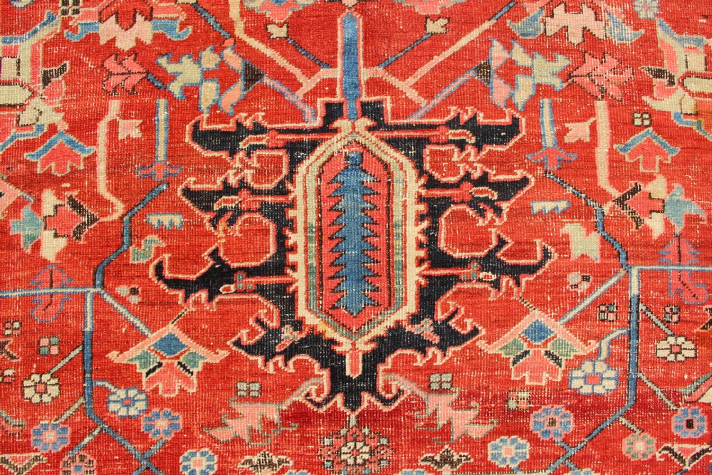 An antique Persian Bakshaish wool carpet featuring a terracotta red field with geometric central motifs enclosed by a light blue patterned border. View IX