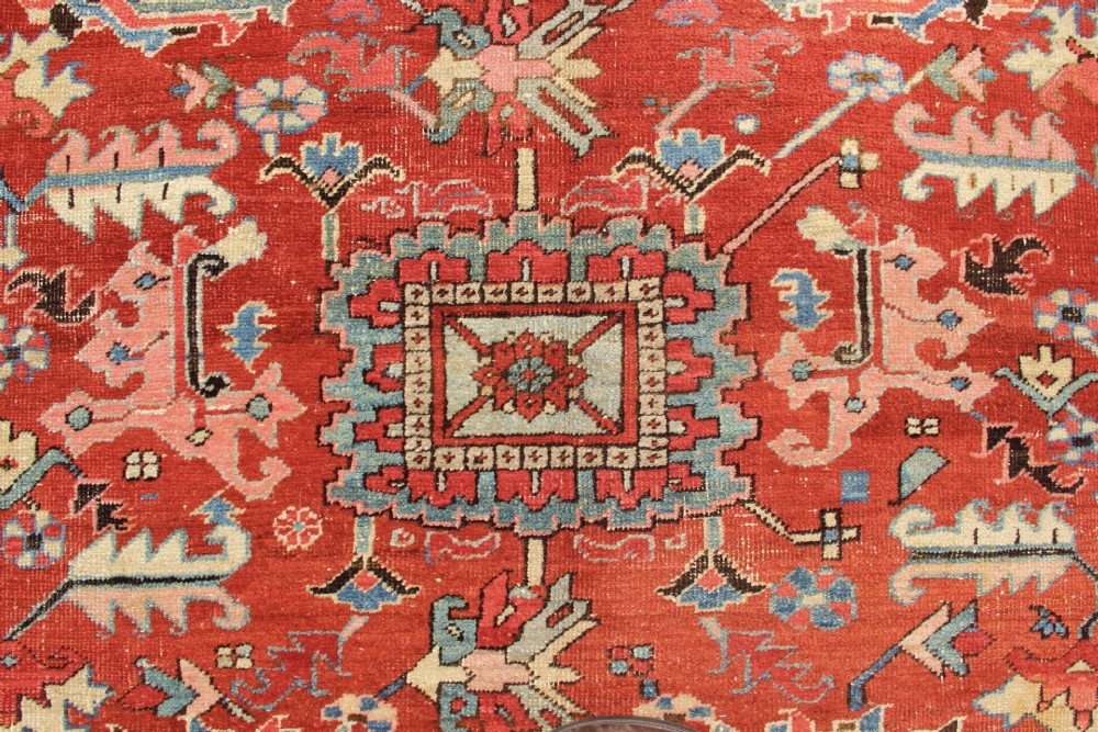 An antique Persian Bakshaish wool carpet featuring a terracotta red field with geometric central motifs enclosed by a light blue patterned border. View XI