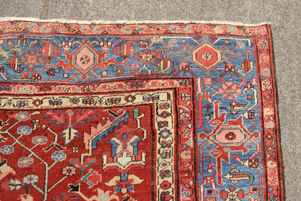 An antique Persian Bakshaish wool carpet featuring a terracotta red field with geometric central motifs enclosed by a light blue patterned border. View XII
