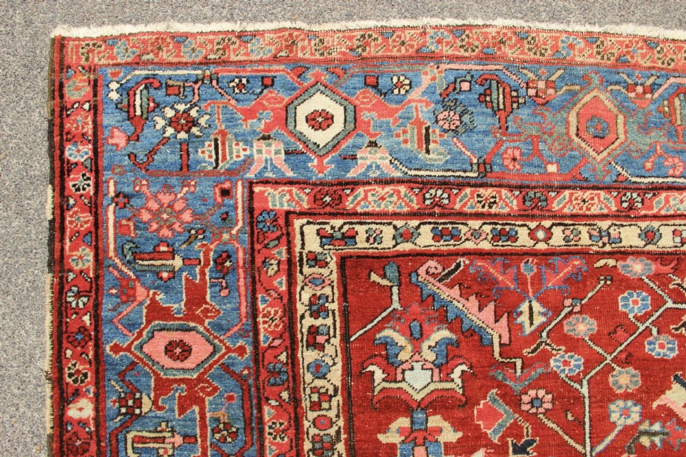 An antique Persian Bakshaish wool carpet featuring a terracotta red field with geometric central motifs enclosed by a light blue patterned border. View XIII