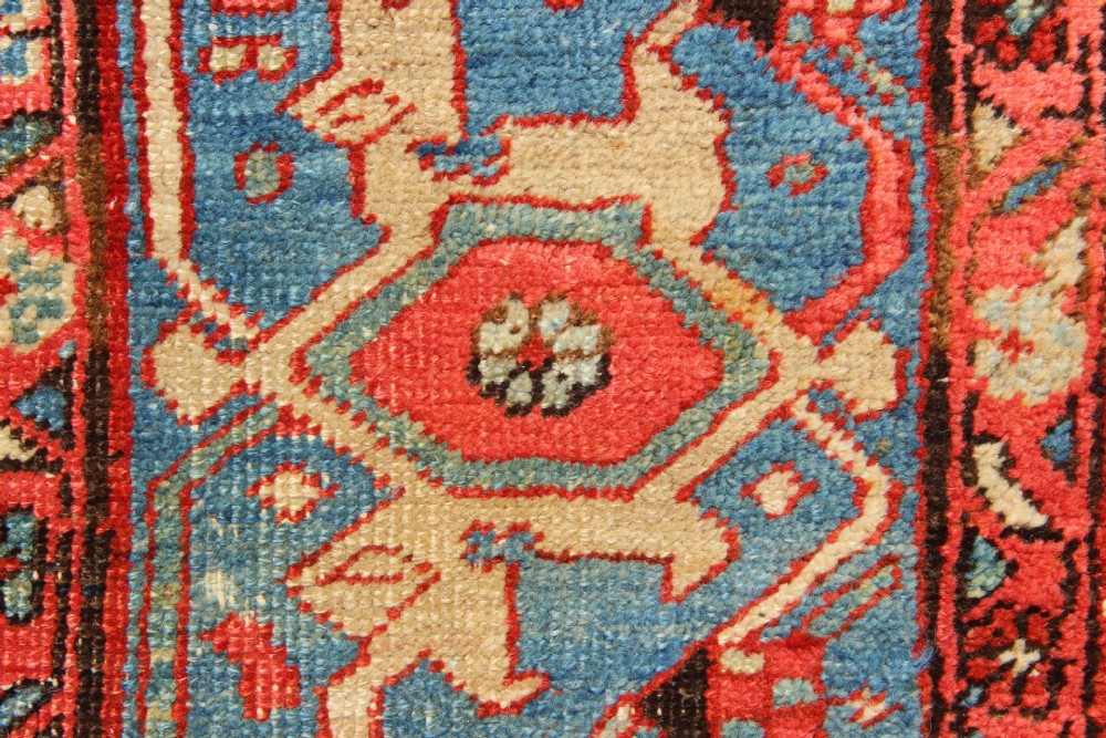An antique Persian Bakshaish wool carpet featuring a terracotta red field with geometric central motifs enclosed by a light blue patterned border. View XV