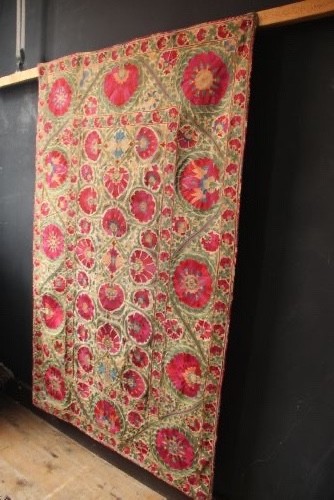 A rectangular hand-embroidered antique Suzani textile featuring red and pink floral medallions on a cream background with green vine borders. View XI