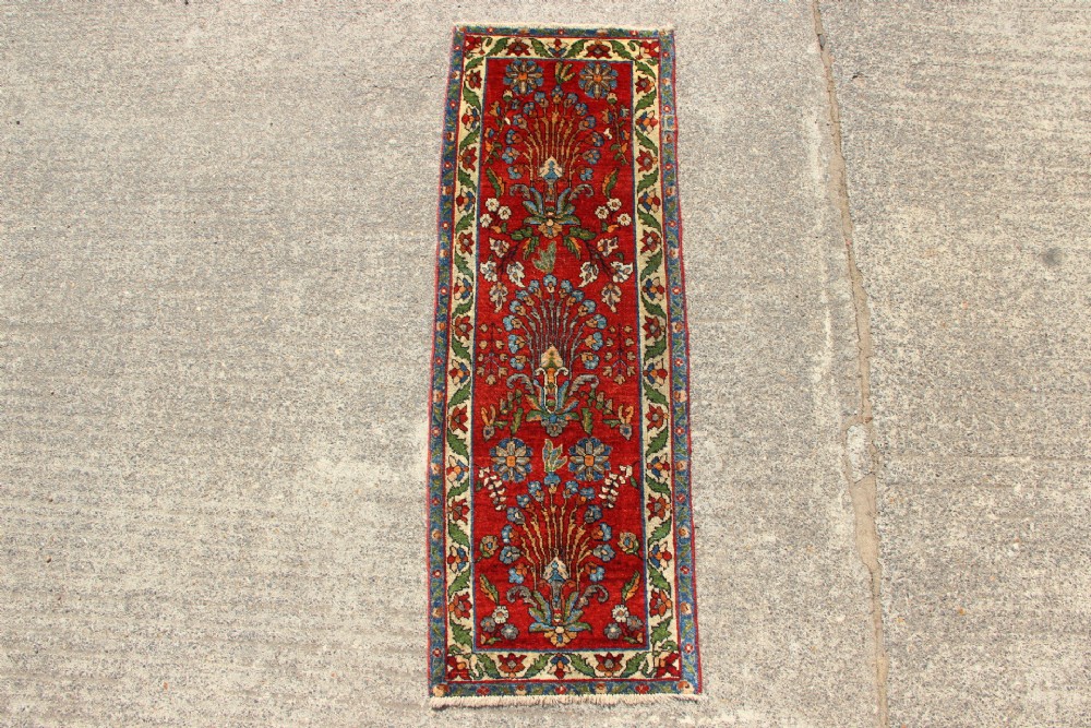 An antique hand-knotted Persian Sarouk rug runner featuring a vibrant crimson field decorated with floral motifs within a patterned border.