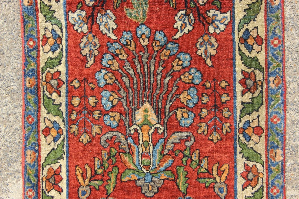An antique hand-knotted Persian Sarouk rug runner featuring a vibrant crimson field decorated with floral motifs within a patterned border. View III