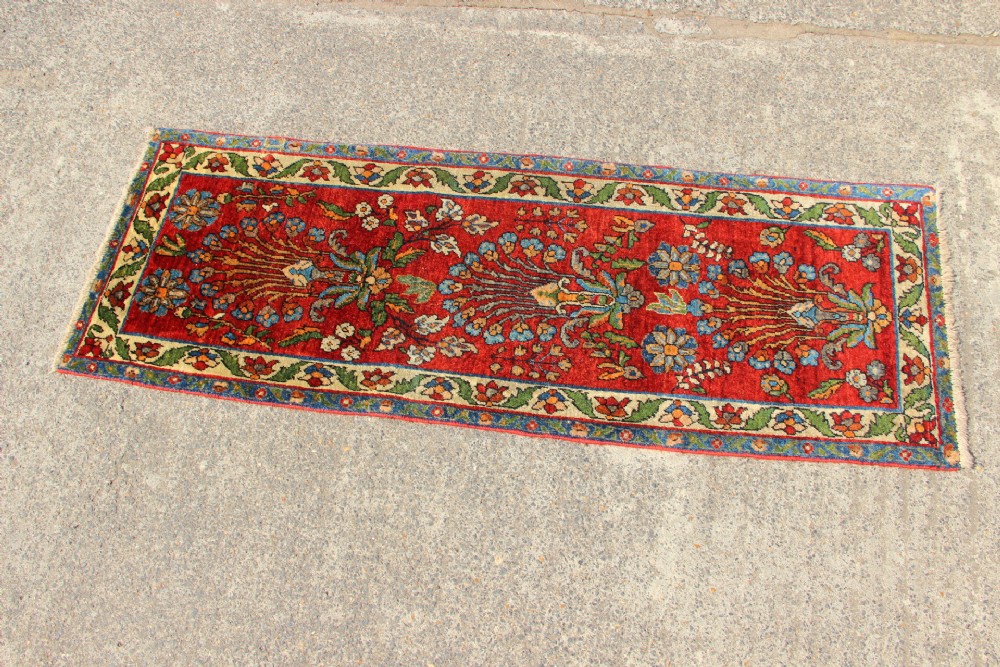An antique hand-knotted Persian Sarouk rug runner featuring a vibrant crimson field decorated with floral motifs within a patterned border. View V