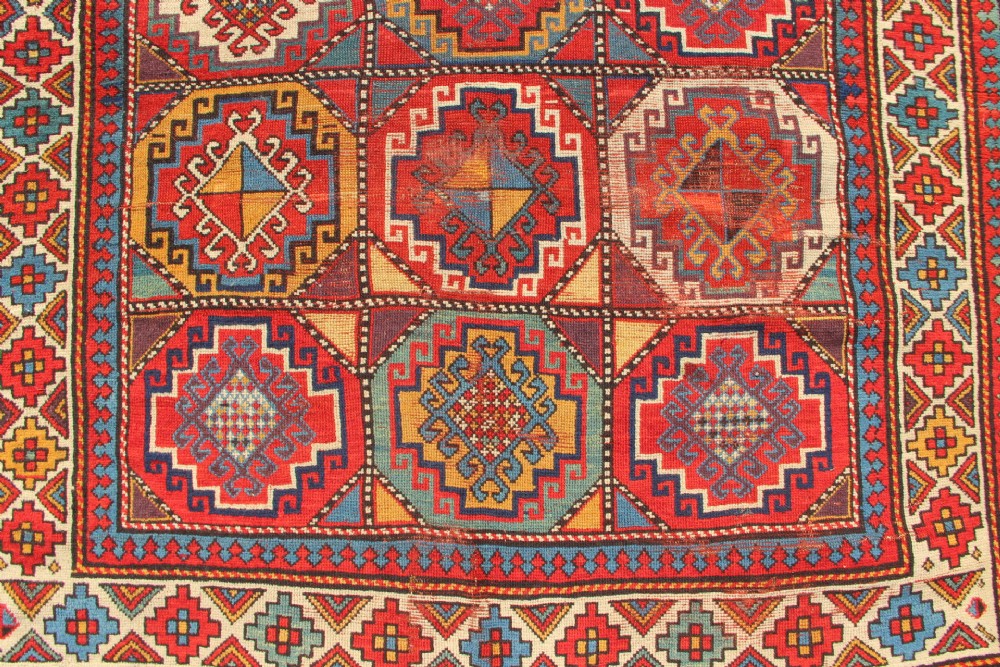 An antique Caucasian Moghan Kazak hand-knotted wool carpet displaying geometric octagonal medallions in red, blue, cream, and ochre yellow shades. View II