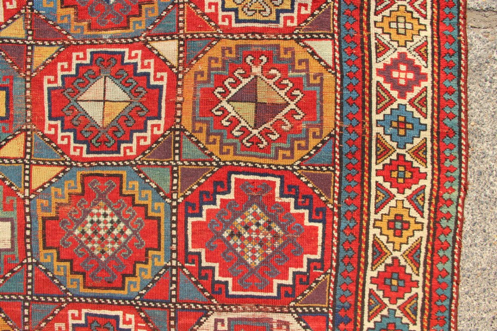 An antique Caucasian Moghan Kazak hand-knotted wool carpet displaying geometric octagonal medallions in red, blue, cream, and ochre yellow shades. View III