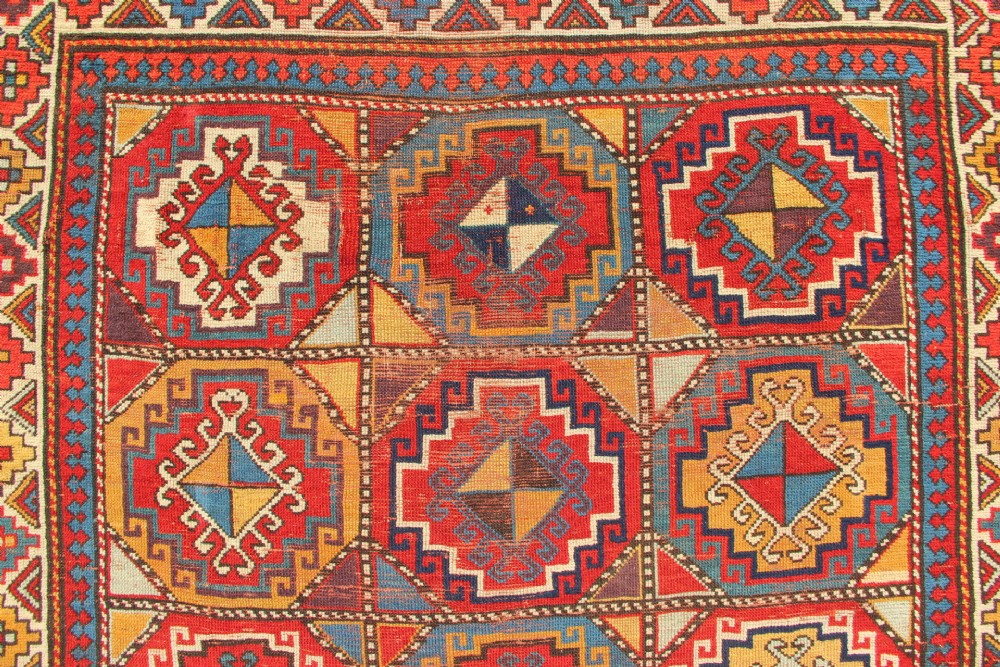 An antique Caucasian Moghan Kazak hand-knotted wool carpet displaying geometric octagonal medallions in red, blue, cream, and ochre yellow shades. View IV