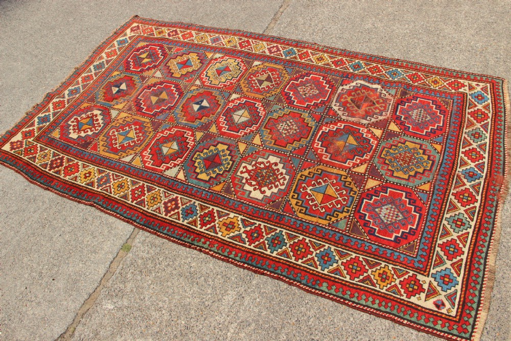 An antique Caucasian Moghan Kazak hand-knotted wool carpet displaying geometric octagonal medallions in red, blue, cream, and ochre yellow shades. View VI