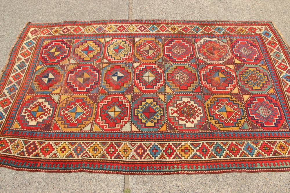 An antique Caucasian Moghan Kazak hand-knotted wool carpet displaying geometric octagonal medallions in red, blue, cream, and ochre yellow shades. View VII