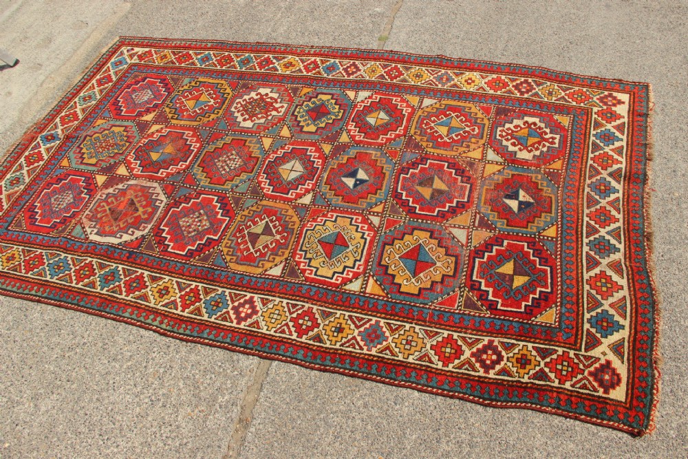 An antique Caucasian Moghan Kazak hand-knotted wool carpet displaying geometric octagonal medallions in red, blue, cream, and ochre yellow shades. View VIII