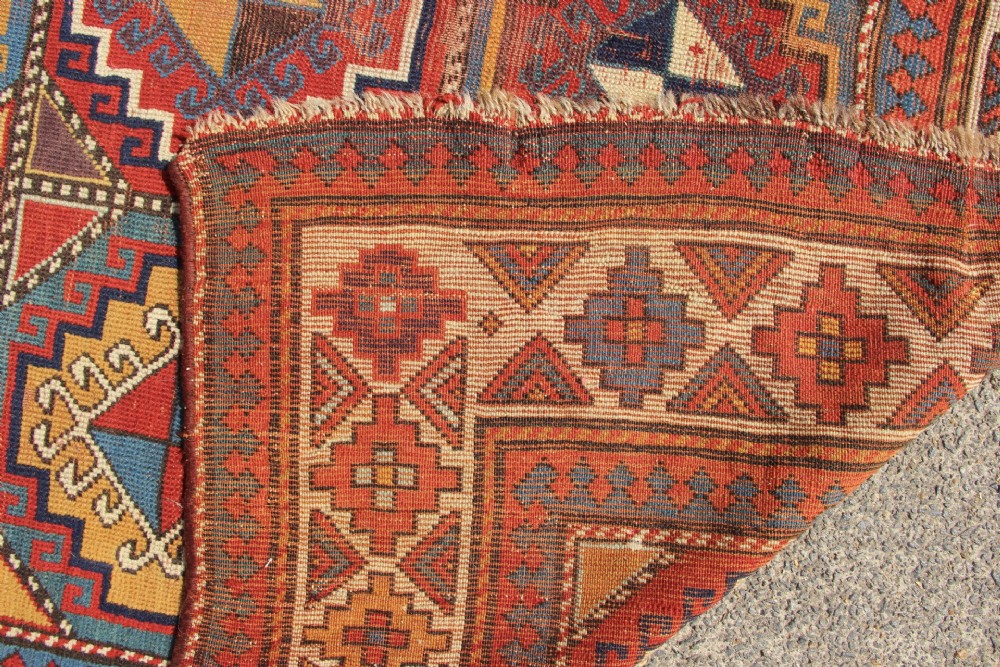An antique Caucasian Moghan Kazak hand-knotted wool carpet displaying geometric octagonal medallions in red, blue, cream, and ochre yellow shades. View IX