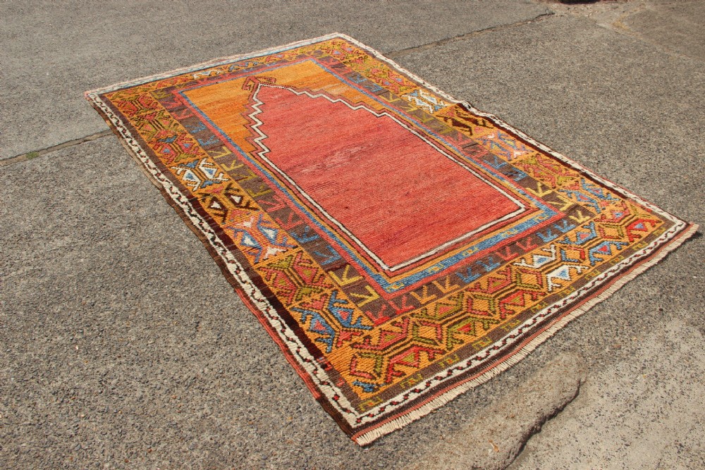 A hand-knotted mid-19th-century Konya prayer rug featuring a central red stepped mihrab motif surrounded by geometric patterned borders in ochre yellow, brown, and blue tones. View II