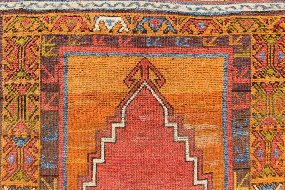 A hand-knotted mid-19th-century Konya prayer rug featuring a central red stepped mihrab motif surrounded by geometric patterned borders in ochre yellow, brown, and blue tones. View III