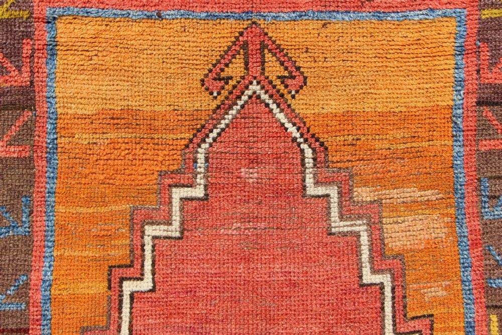 A hand-knotted mid-19th-century Konya prayer rug featuring a central red stepped mihrab motif surrounded by geometric patterned borders in ochre yellow, brown, and blue tones. View IV