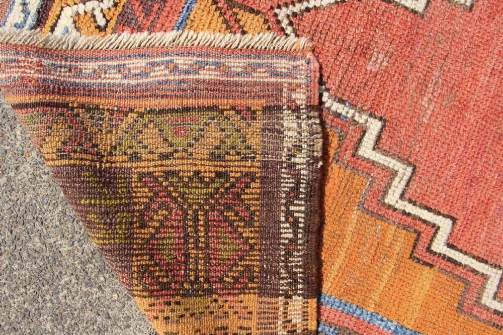 A hand-knotted mid-19th-century Konya prayer rug featuring a central red stepped mihrab motif surrounded by geometric patterned borders in ochre yellow, brown, and blue tones. View VII