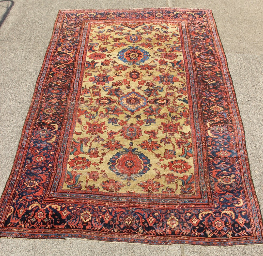 An antique hand-knotted Fereghan Persian carpet featuring a central cream field filled with red and navy floral motifs framed by a wide geometric border.