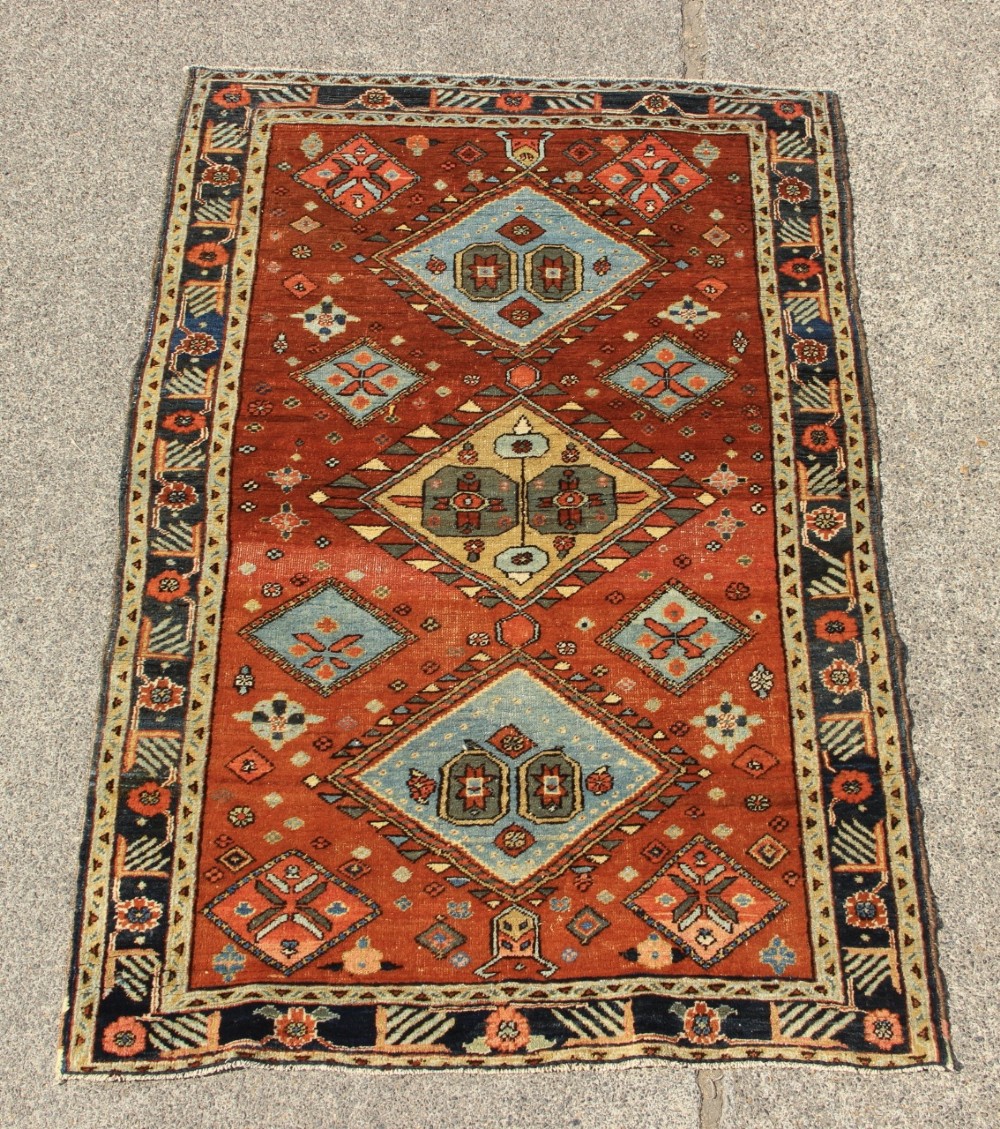 An antique hand-knotted Heriz rug featuring geometric diamond medallions in blue and yellow set against a rust-red ground with a patterned dark border.