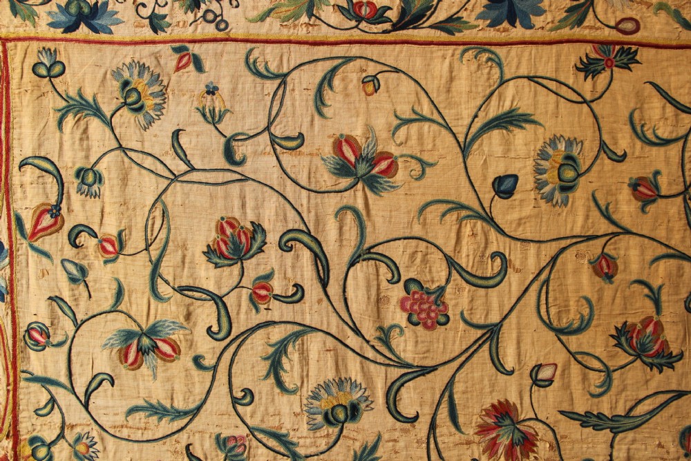A large rectangular antique English crewelwork panel with intricate hand-embroidered floral tendrils in green, blue, and red wool on a cream background. View III