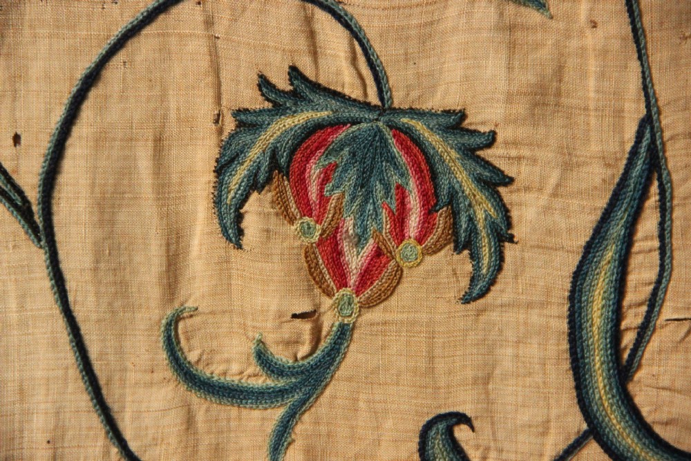 A large rectangular antique English crewelwork panel with intricate hand-embroidered floral tendrils in green, blue, and red wool on a cream background. View VI
