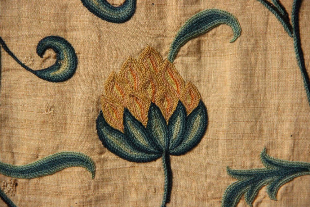 A large rectangular antique English crewelwork panel with intricate hand-embroidered floral tendrils in green, blue, and red wool on a cream background. View VII