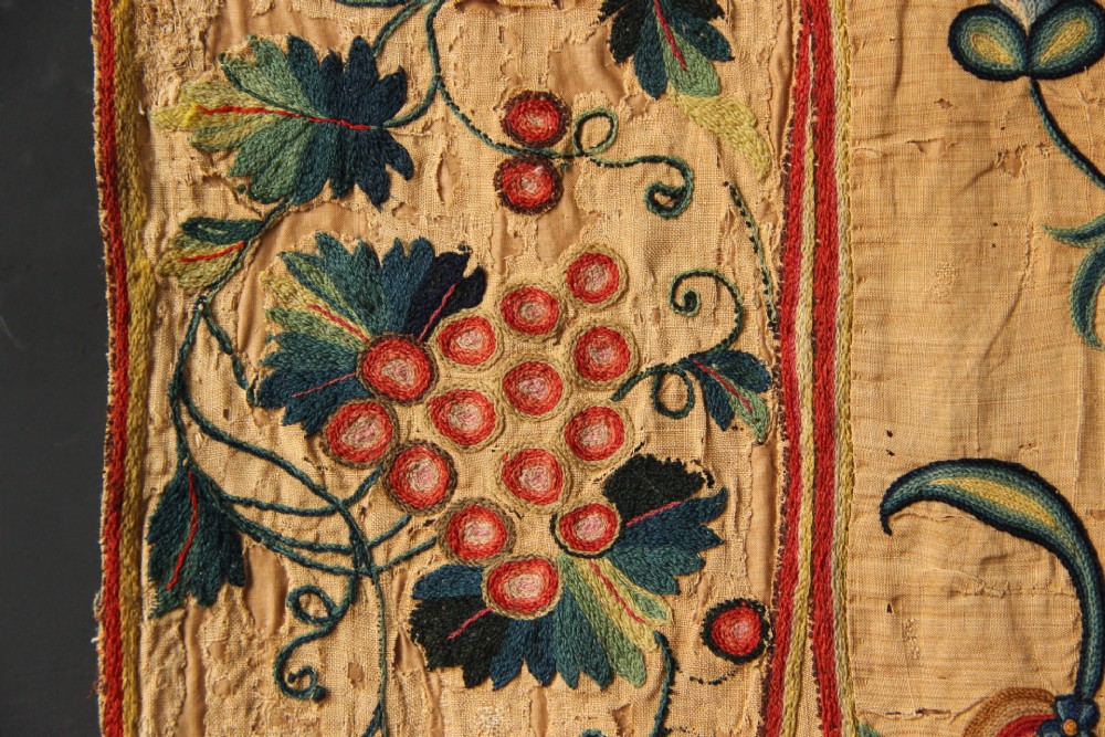 A large rectangular antique English crewelwork panel with intricate hand-embroidered floral tendrils in green, blue, and red wool on a cream background. View IX