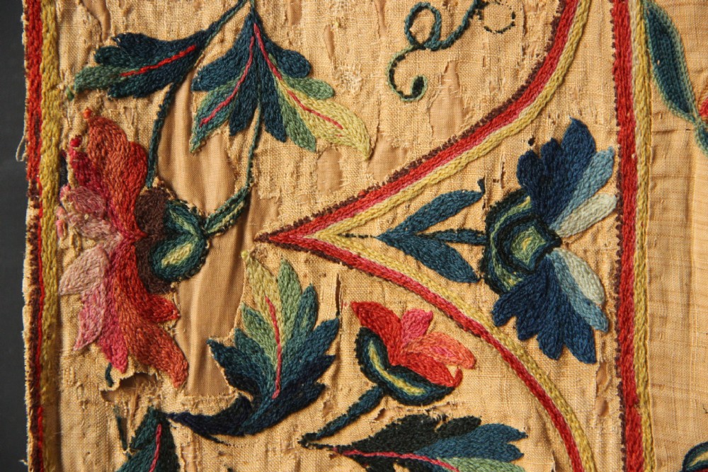 A large rectangular antique English crewelwork panel with intricate hand-embroidered floral tendrils in green, blue, and red wool on a cream background. View X