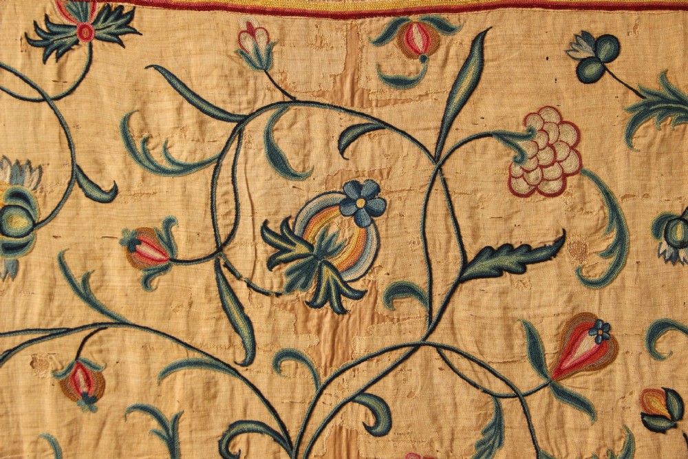 A large rectangular antique English crewelwork panel with intricate hand-embroidered floral tendrils in green, blue, and red wool on a cream background. View XI