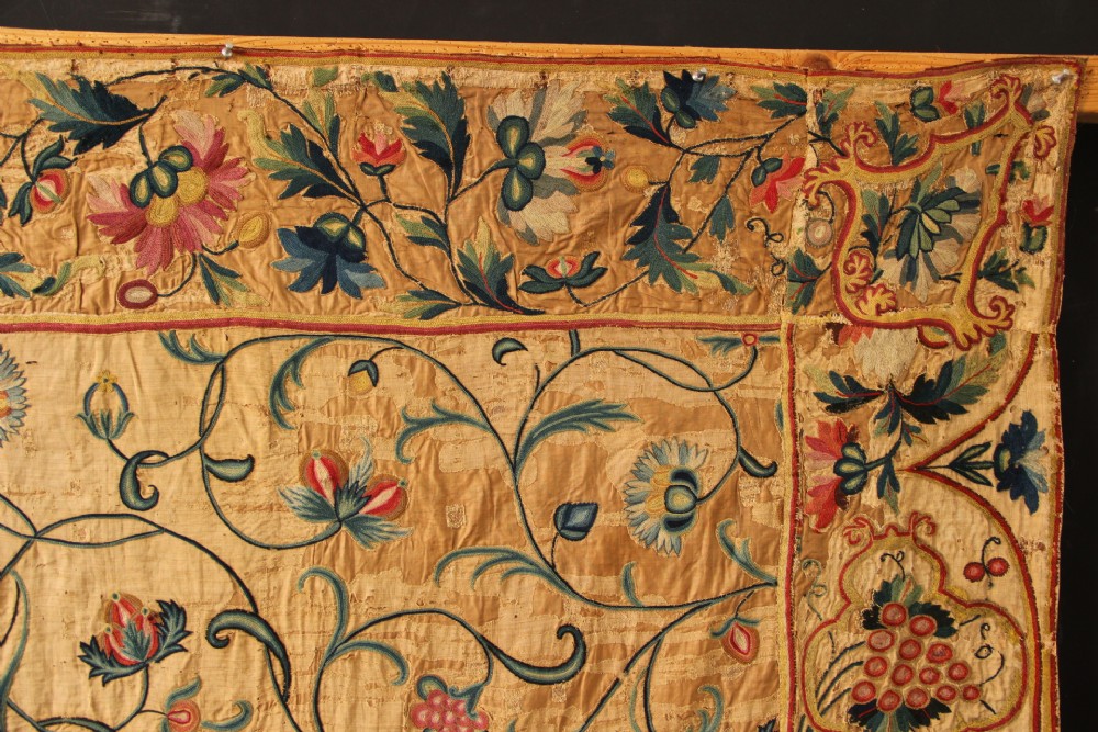 A large rectangular antique English crewelwork panel with intricate hand-embroidered floral tendrils in green, blue, and red wool on a cream background. View XII