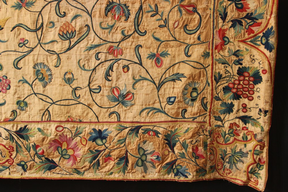 A large rectangular antique English crewelwork panel with intricate hand-embroidered floral tendrils in green, blue, and red wool on a cream background. View XIII