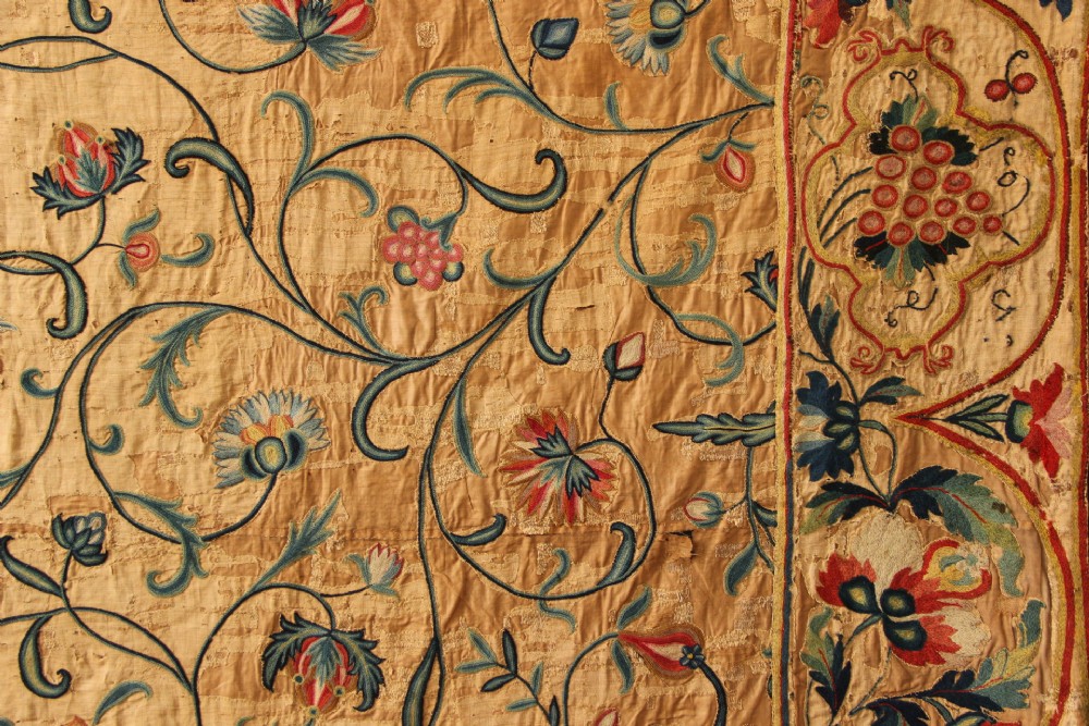 A large rectangular antique English crewelwork panel with intricate hand-embroidered floral tendrils in green, blue, and red wool on a cream background. View XIV