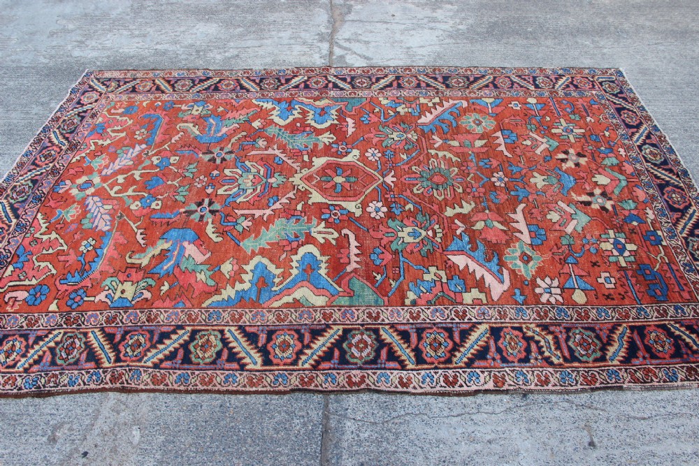 An antique hand-knotted Heriz carpet featuring a terracotta red field with central geometric motifs and a navy blue patterned border. View II