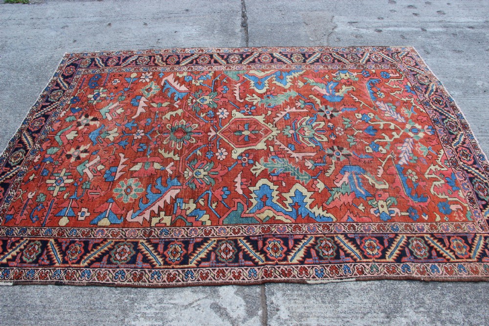 An antique hand-knotted Heriz carpet featuring a terracotta red field with central geometric motifs and a navy blue patterned border. View VI