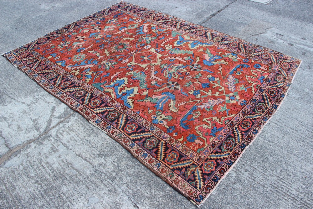 An antique hand-knotted Heriz carpet featuring a terracotta red field with central geometric motifs and a navy blue patterned border. View VII
