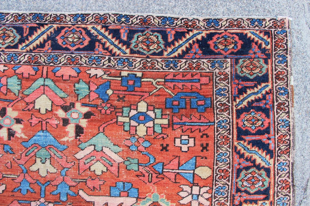 An antique hand-knotted Heriz carpet featuring a terracotta red field with central geometric motifs and a navy blue patterned border. View IX