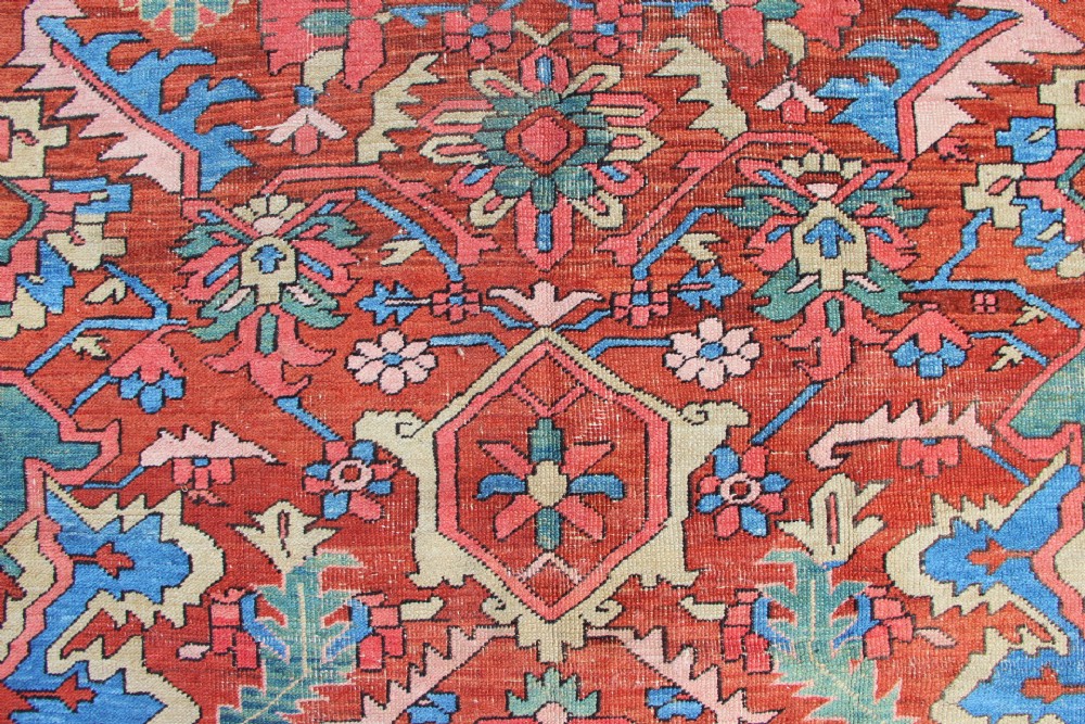 An antique hand-knotted Heriz carpet featuring a terracotta red field with central geometric motifs and a navy blue patterned border. View X