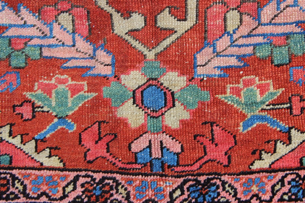 An antique hand-knotted Heriz carpet featuring a terracotta red field with central geometric motifs and a navy blue patterned border. View XI