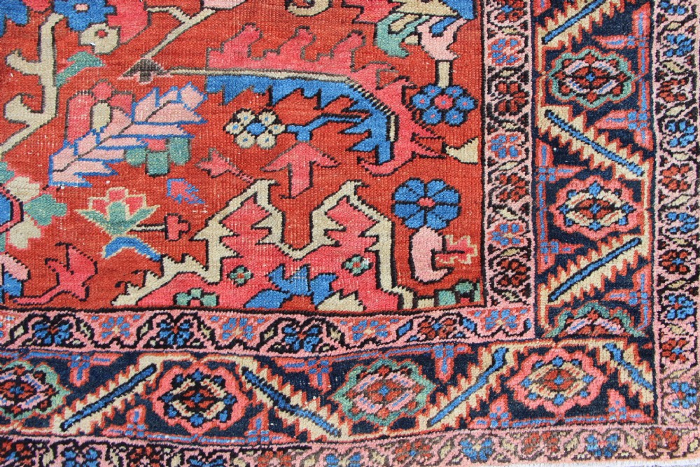 An antique hand-knotted Heriz carpet featuring a terracotta red field with central geometric motifs and a navy blue patterned border. View XII