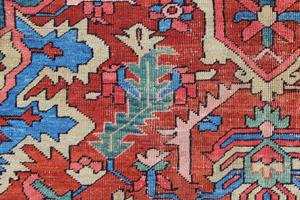 An antique hand-knotted Heriz carpet featuring a terracotta red field with central geometric motifs and a navy blue patterned border. View XIII